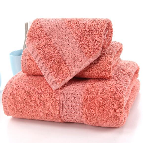 Set of three coral pink eprolo 100% cotton terry bath towels folded in a stack.