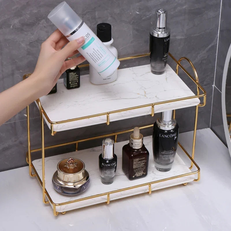 Golden double-layer iron cosmetic storage rack with marble shelves holding skincare bottles.