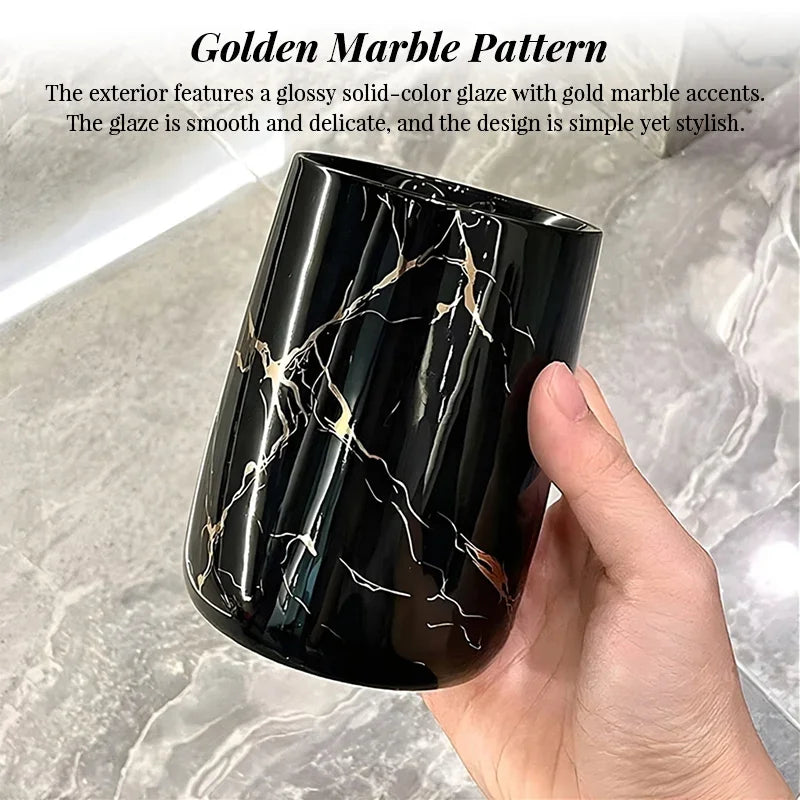 Black ceramic bathroom tumbler with a glossy golden marble pattern held by a hand.
