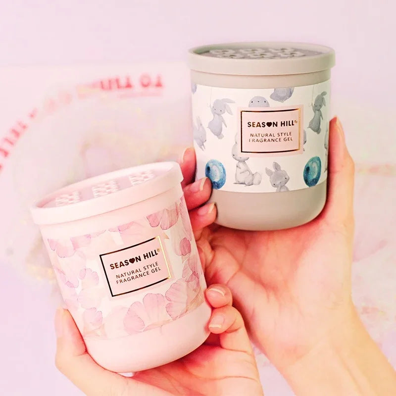 Two Season Hill Natural Style Fragrance Gel containers in pink and grey held by hands.